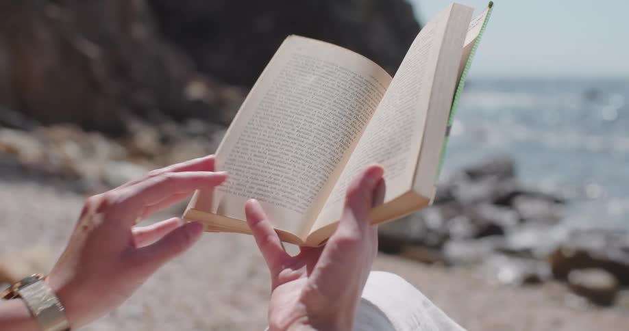 Hands holding a book by the sea