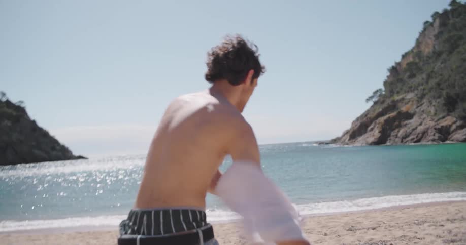 A young man takes of his clothes inviting his girlfriend to swim on the beach