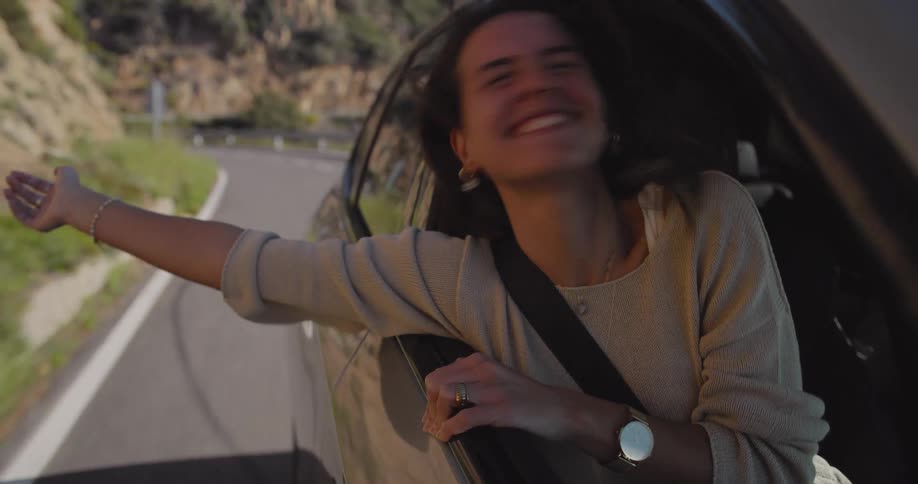 A woman leaning out of a cars passenger side enjoying a road trip