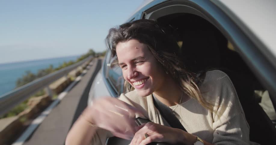 Woman with her arms out of a moving car enjoying the moment in a natural environment by the sea