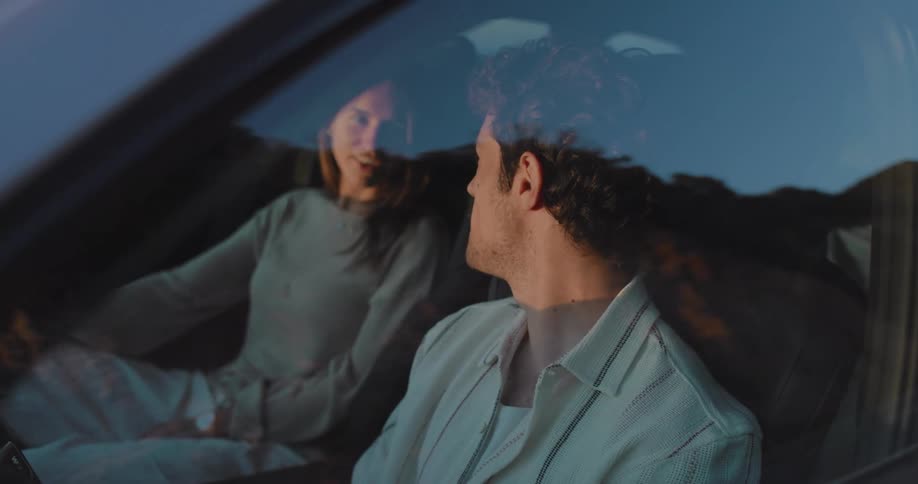 A young couple seated inside a vehicle turn to look at each other