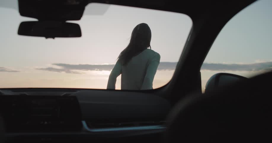 Woman getting out of the car towards the hood and her boyfriend hugs him while they enjoy the view of the sunset