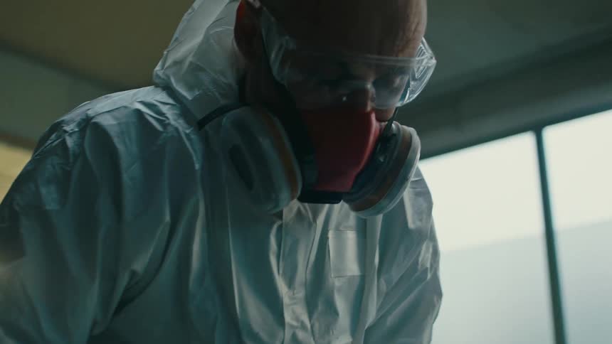 An individual in a white protective suit is finishing a metallic blue car part