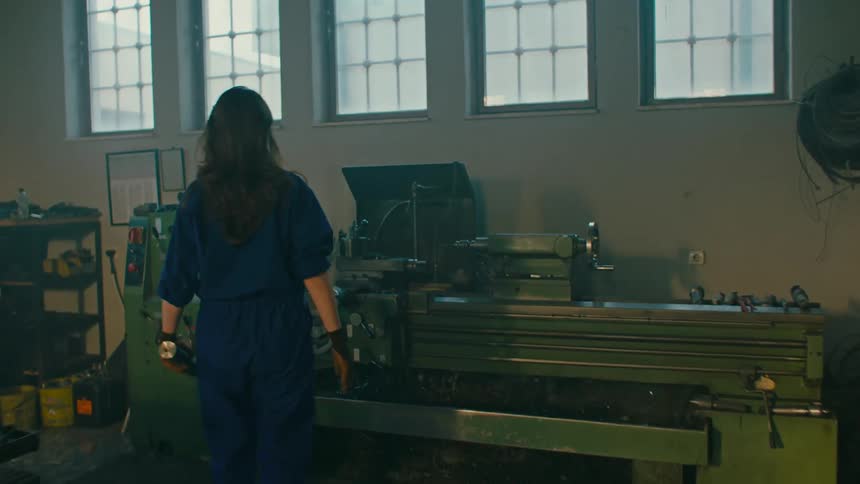 Woman inside a factory in a blue coat placing a cylinder inside a machine
