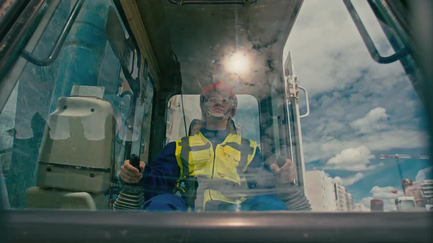 An woman wearing a yellow highvisibility jacket and a red hard hat operating heavy machinery