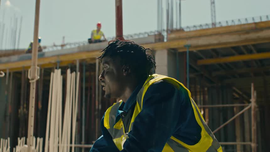 Hardworking construction worker wearing a safety vest and helmet at a construction site drinking water on a sunny day