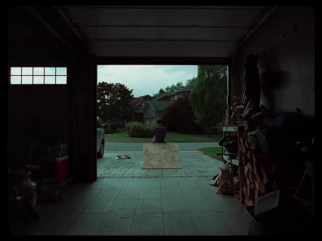 A boy dragging a plank of wood from a garage at morning