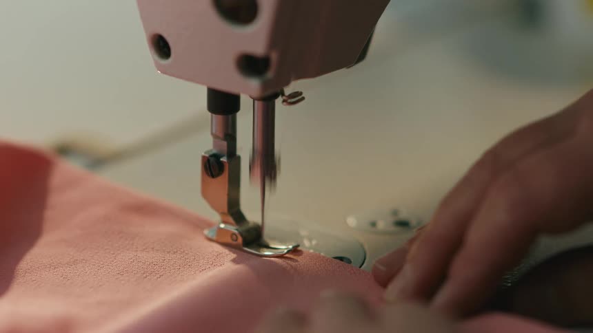 Closeup on a machine sewing a pink fabric with the help of a womans hands