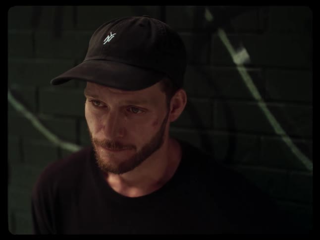 Man with a beard and cap leaning against the wall with his eyes watering