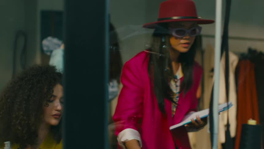 Woman wearing a pink look giving instructions to two seamstresses inside a clothing store