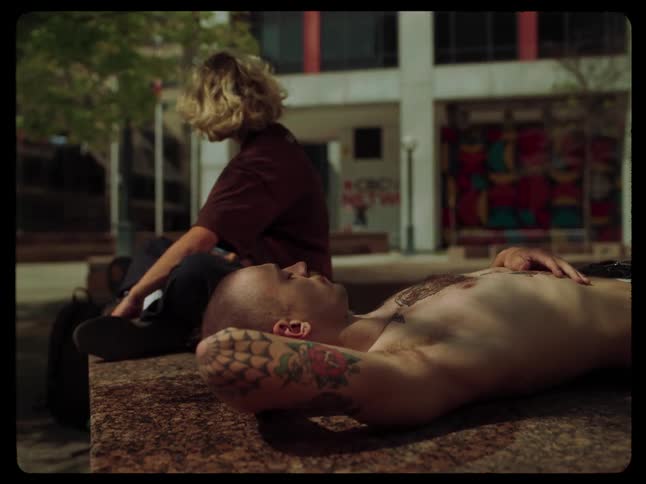 A woman sits next to a shirtless man with tattooed arms