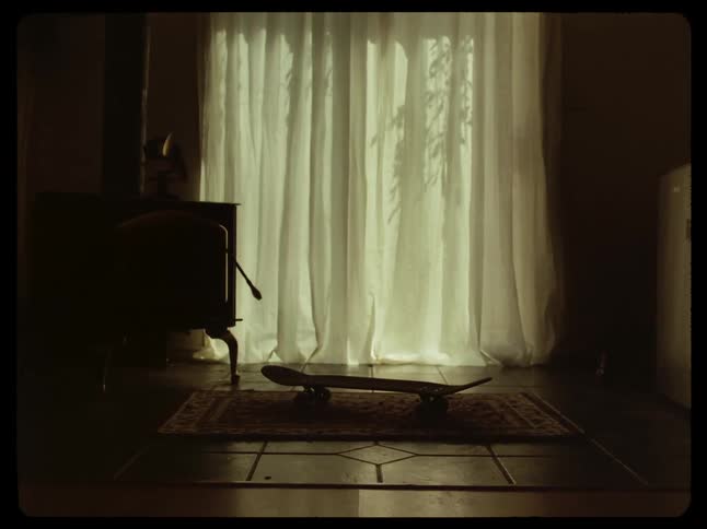 Skateboard in a room on a rug next to a vintage oven and a curtain in the background