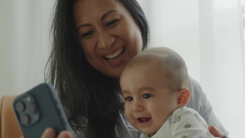 Portrait of mother holding her baby on her lap and taking a selfie with a smartphone