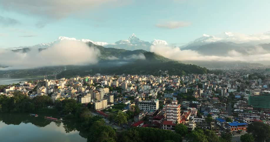 The urban landscape unfolds along the coastline with a picturesque lake reflecting the city lights and a backdrop of snowcapped mountains