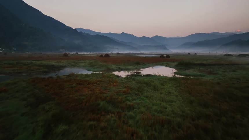 Aerial panorama of a calm lake with a person riding a canoe and the silhouette of mountains on the horizon against a reddish sky