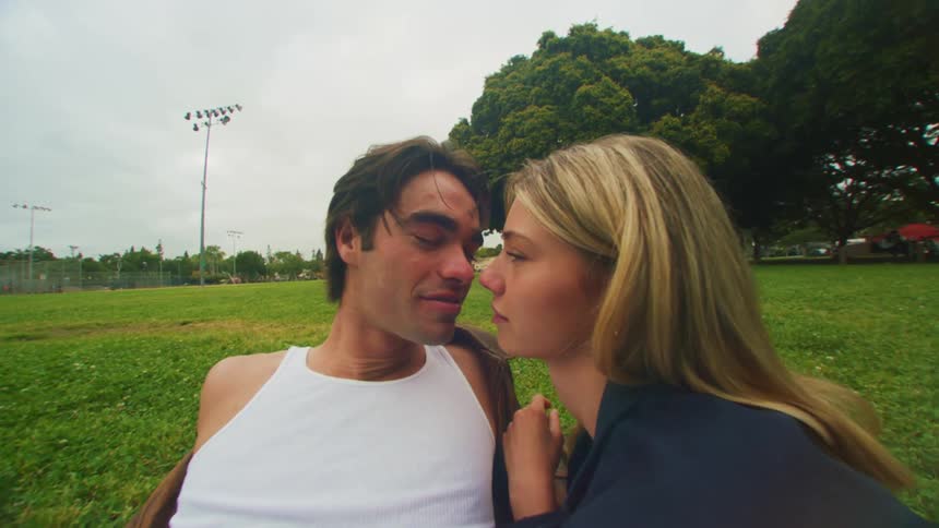 Couple lying together on the ground in a large field kiss