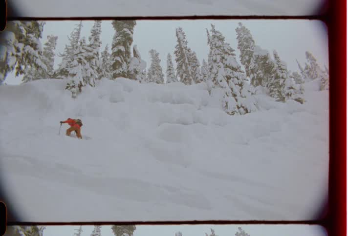 A skier wearing orange clothes climbs a snow covered slope caught on vintage film