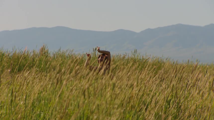 Man without a shirt dancing on a hill in the middle of vegetation during the day