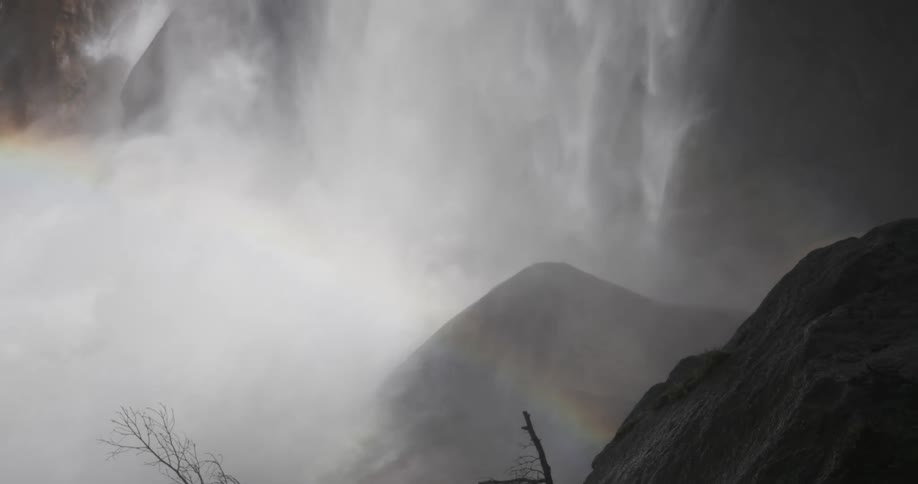 The cascading water of the waterfall creates a veil of mist that softens the dark rocks below