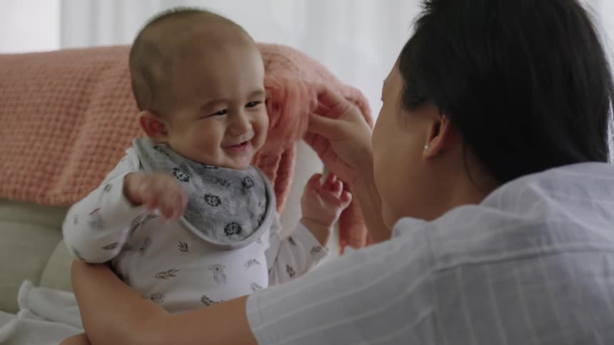 Mother playing with her baby with a blanket on the sofa