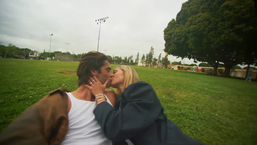 A young couple laying in the grass on a park kissing