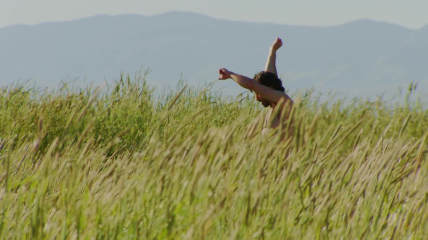 Man without a shirt spinning while dancing on a hill with vegetation around him