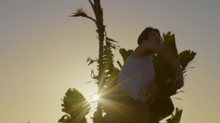 Man in white tank top dancing against the reflection of the morning sun