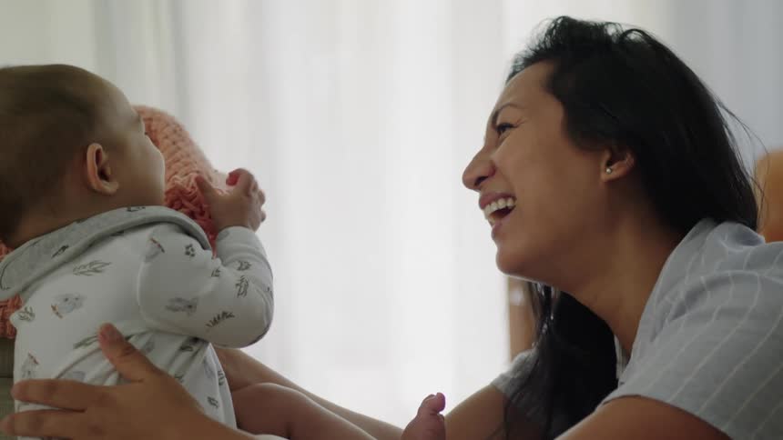 A woman holding a baby playing with them as both laugh