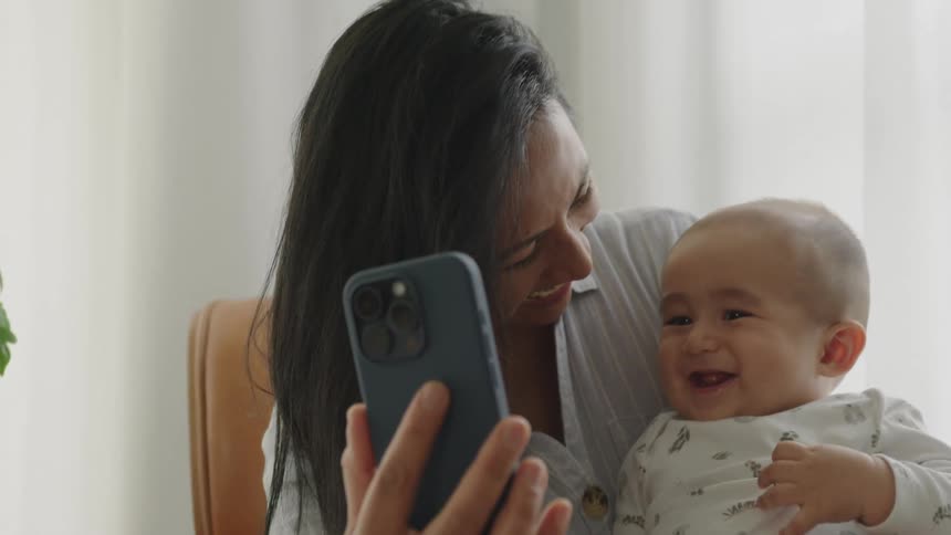 Portrait of a smiling mother holding her baby on her lap while also holding an iphone
