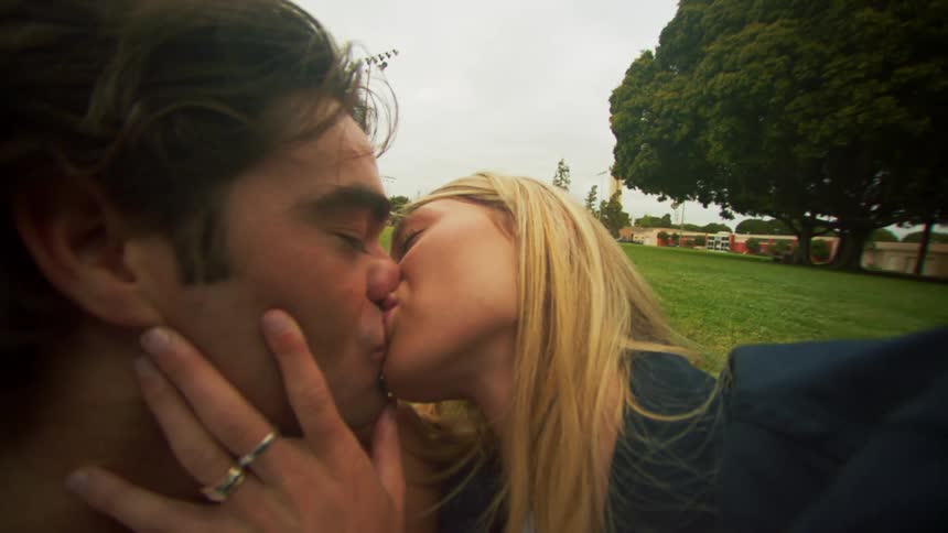 A couple kissing while sitting in grass in a park
