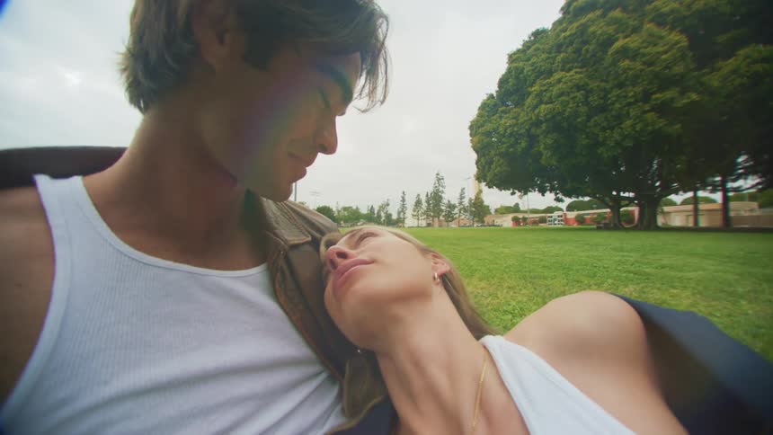 A man and a woman kissing while lying on the grass in a park
