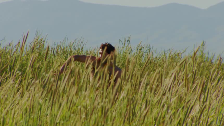 Man without a shirt dancing on a hill with vegetation around him