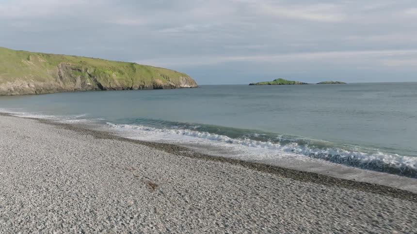 The beach is deserted under a clear blue sky with fluffy white waves rolling in towards the shore