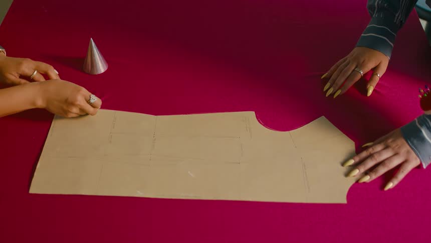 A fashion designer tracing clothes patterns over a red fabric