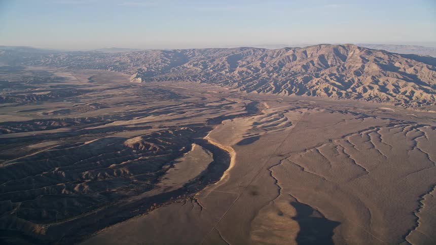 An aerial view of a vast arid landscape with bare mountains and dry river beds