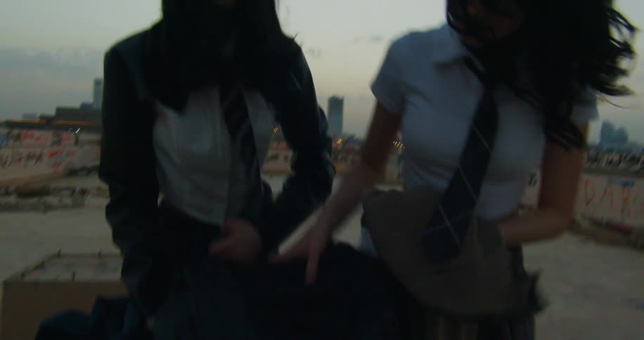 Two individuals in school uniforms handle pieces of clothing on a shopping cart in an abandoned parking lot