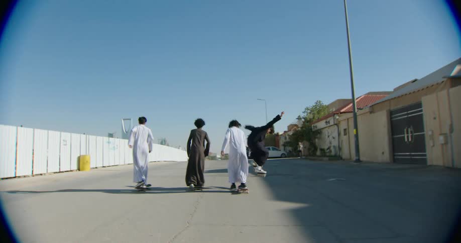 Four boys skateboarding down a paved street