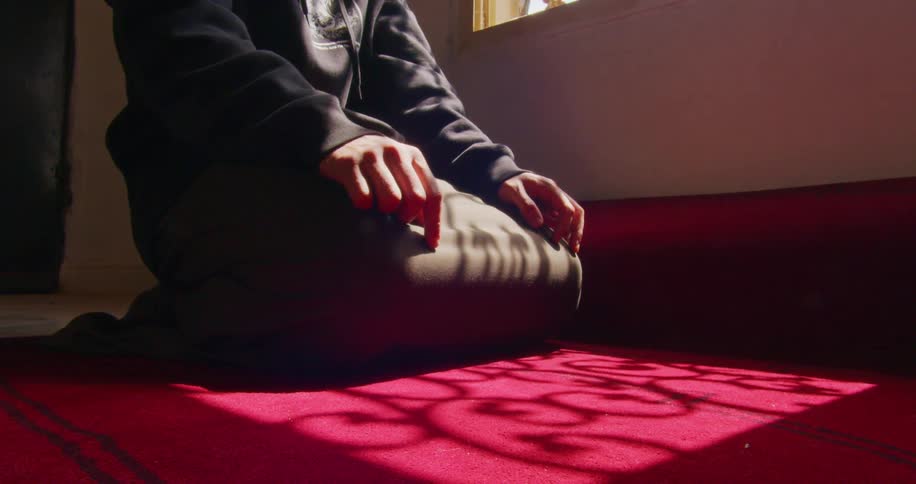 Person kneeling on a red carpet praying