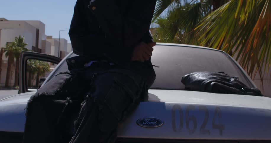 A person smoking a cigarette is seated on the trunk of a car