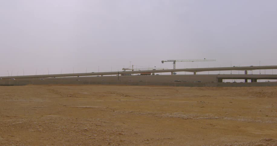 A construction site with an incomplete overpass bridge with cranes against a clear sky