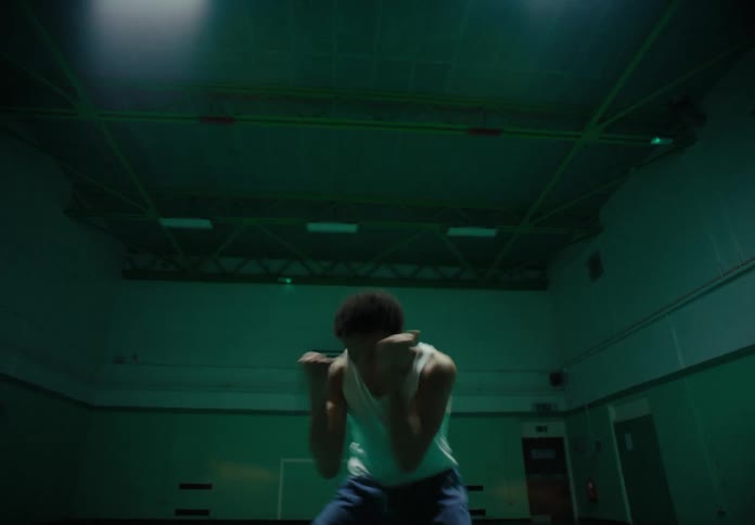 Man wearing a white undershirt an jeans dances in a basketball court