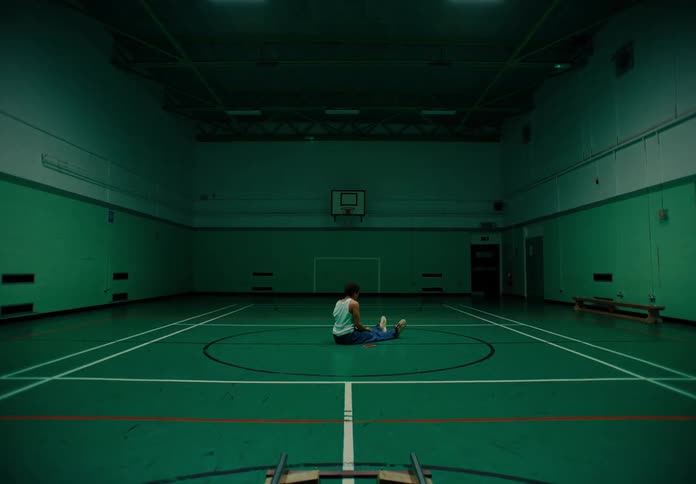Man sitting on the floor of a sports court making movements on his scapula and shoulders