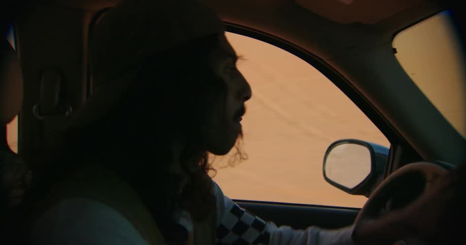 Man with long hair drives a car in the desert