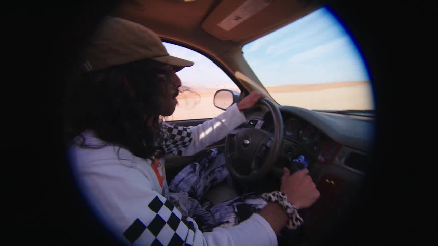 A man inside a car is raising his arm upwards and turning the steering wheel to perform skidding maneuvers