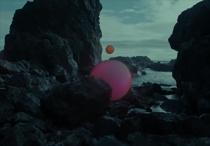 Glowing orange orbs float among dark rocky formations near a misty coastline