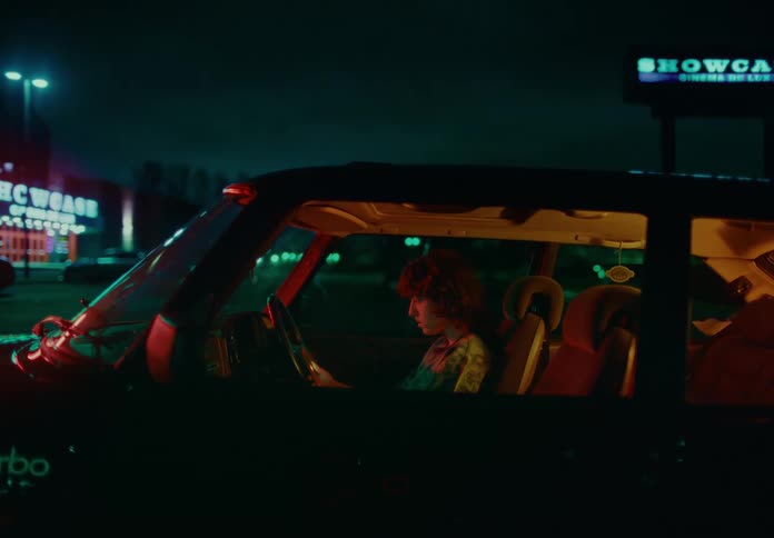 Woman sits reading her smartphone in a car parked in a store parking lot at night