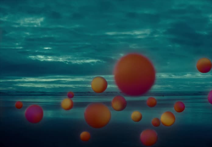 Glowing orange orbs float over the beach near the ocean against the clouds at dusk