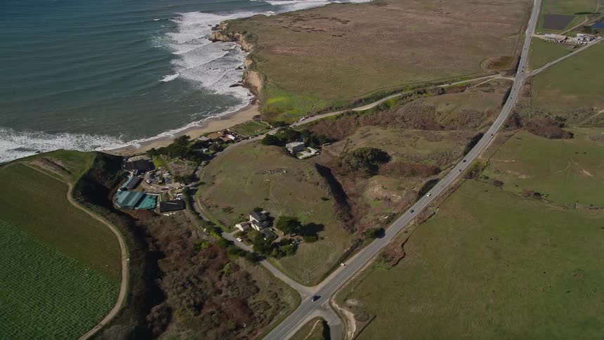 The winding coastal road snakes along the edge of a secluded beach with turquoise water lapping at the shore