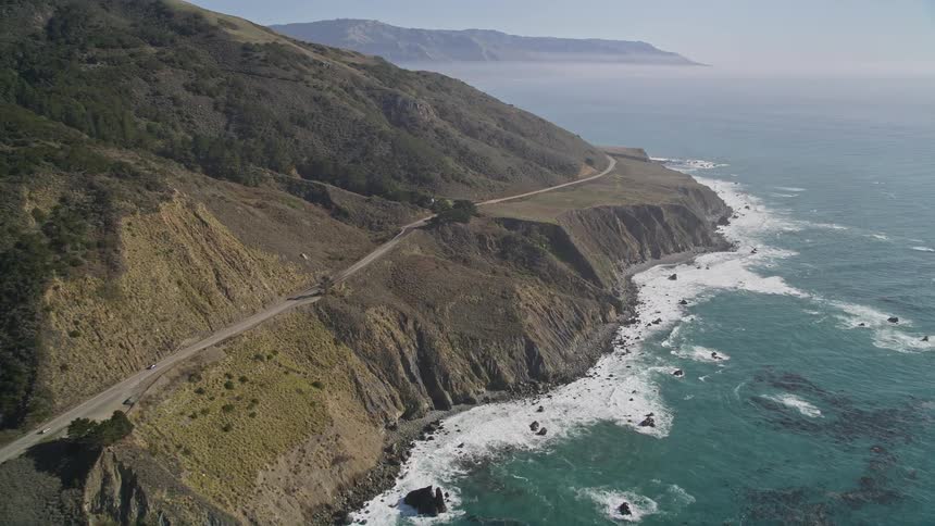 Panorama of greenish mountains with a winding road by the sea