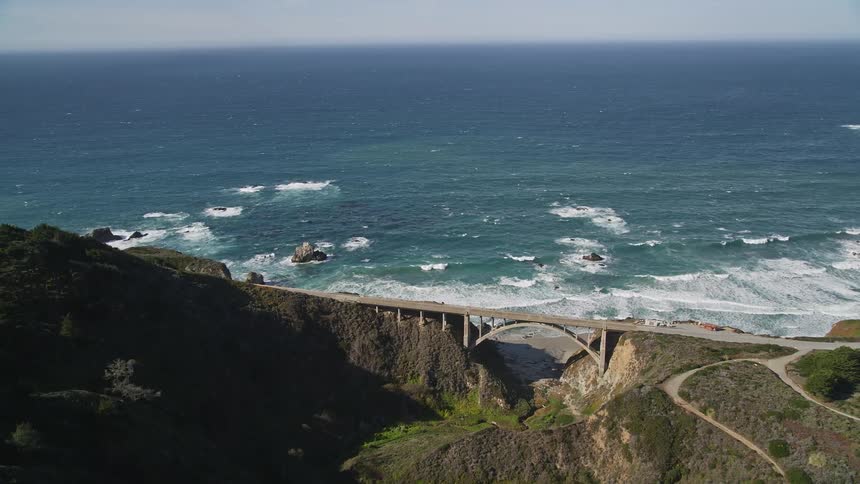 Aerial view of a bridge connecting two seaside mountains during the day